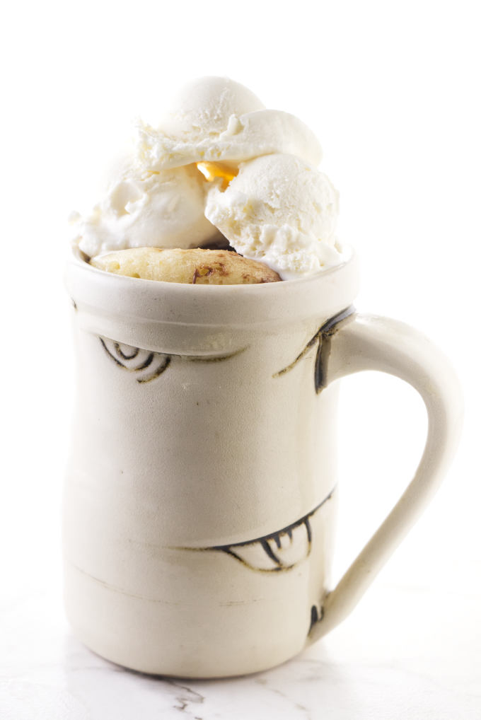 Banana cake in a mug with ice cream piled on top.