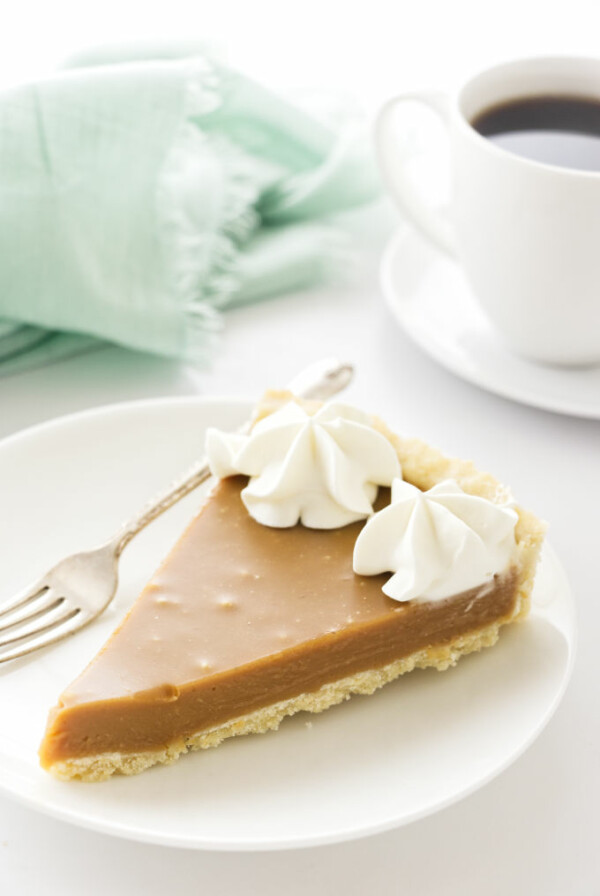 A slice of butterscotch tart with a cup of coffee in the background.