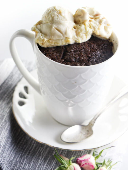 A white mug on a saucer with a chocolate cake baked inside the mug.