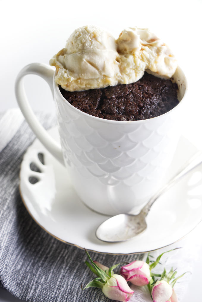 A white mug on a saucer with a chocolate cake baked inside the mug.