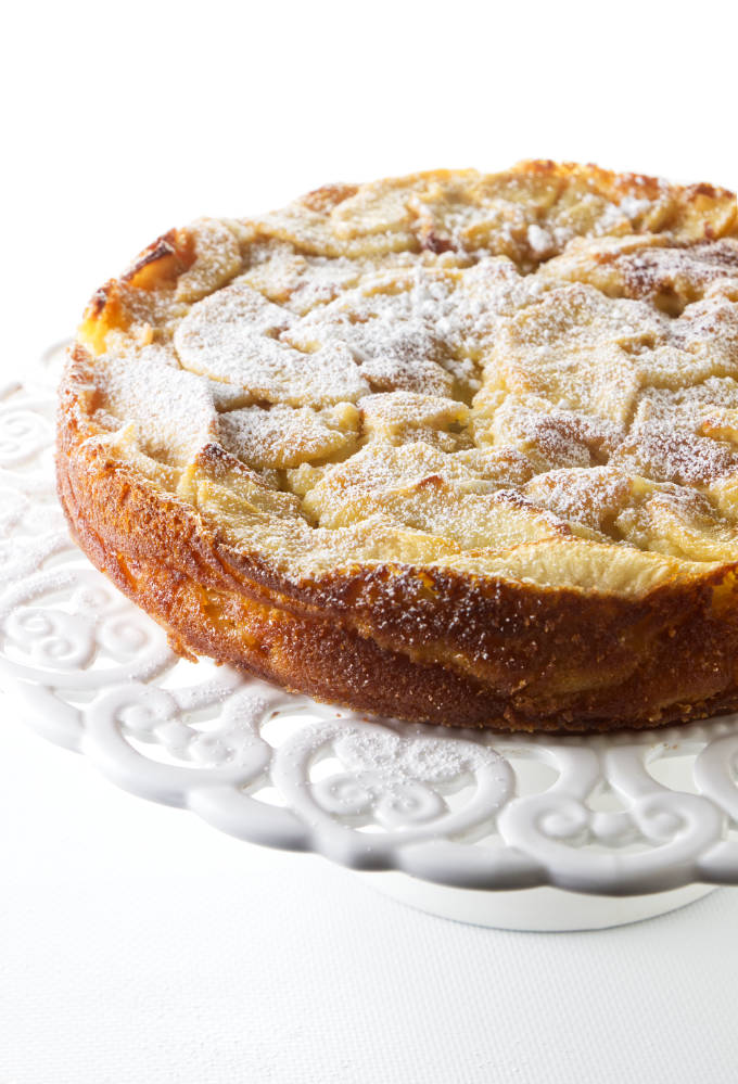 A French apple cake with powdered sugar on a cake platter.