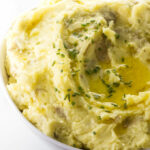 A bowl of mashed potatoes with chives and butter on top.