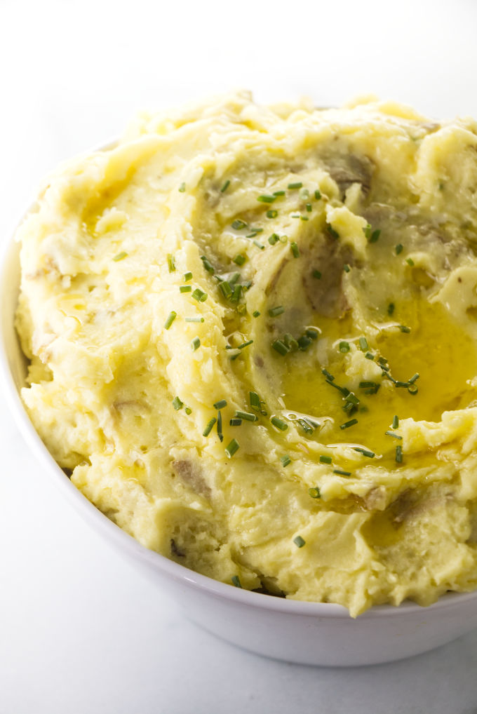 A bowl of mashed potatoes with chives and butter on top.