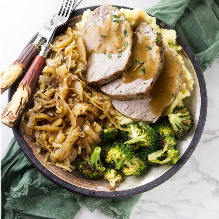 Pork and sauerkraut on a plate with mashed potatoes, gravy, and broccoli.