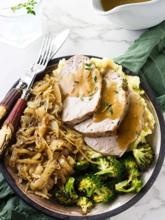A plate with a serving of pork and sauerkraut with a pitcher of gravy on the side.