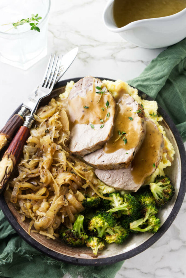 A plate with a serving of pork and sauerkraut with a pitcher of gravy on the side.