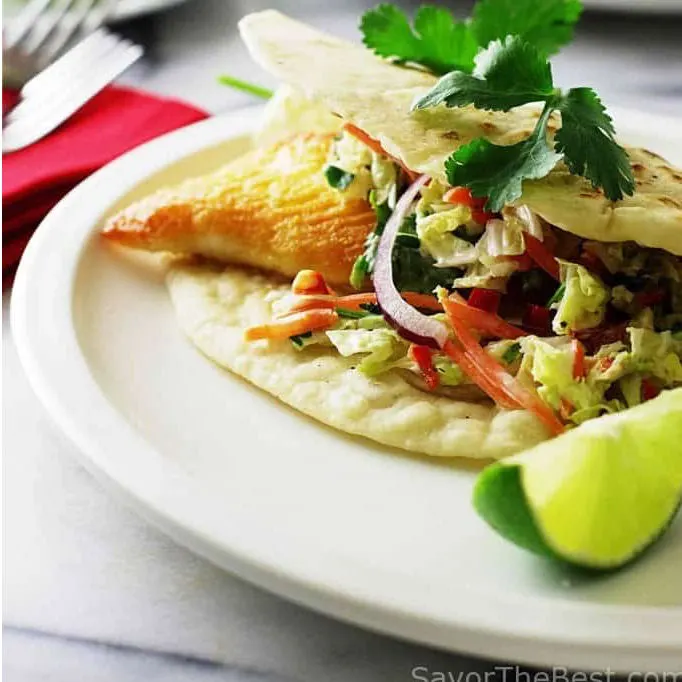 A fish taco on a plate with a slice of lime.