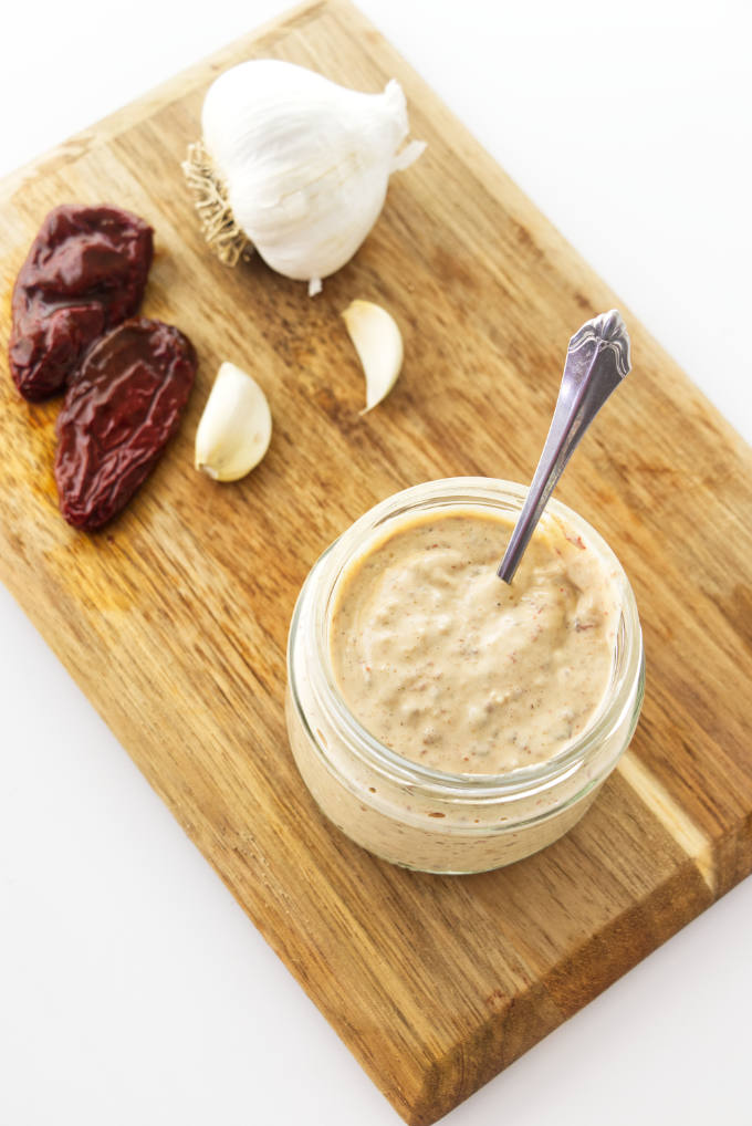 Chipotle aioli in a jar with chipotle peppers and garlic next to it.