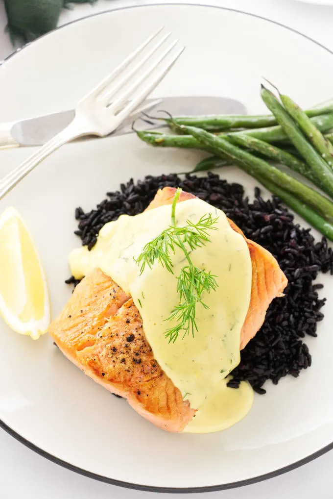Overhead view of pan seared salmon with dill hollandaise sauce, a sprig of fresh dill