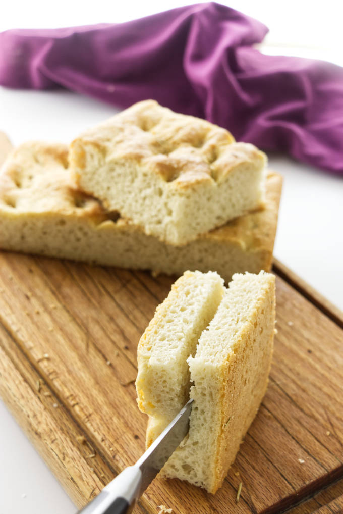 A square of thick, no-knead focaccia bread being sliced in half