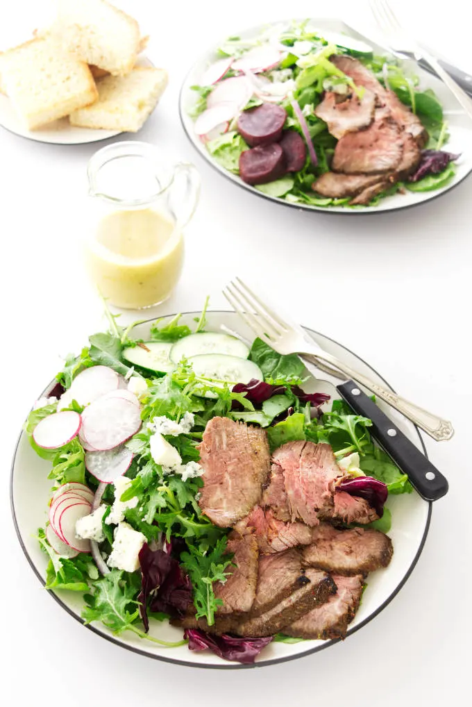 Overhead view of two tri-tip salad servings with dressing on the side