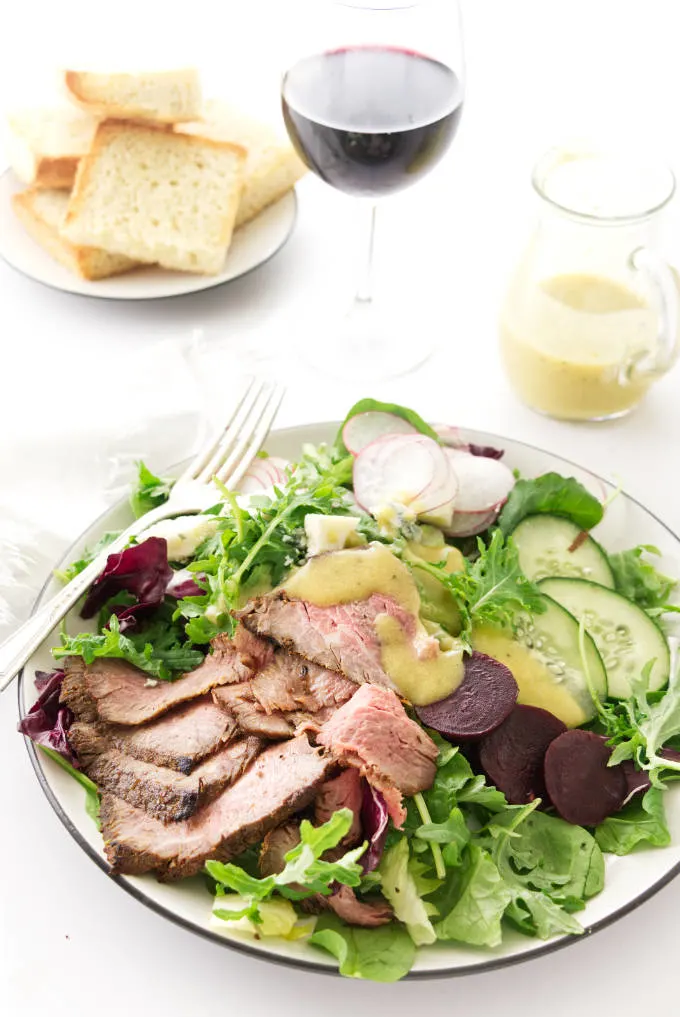 overhead view of a serving of salad, bread, wine and dressing in the background