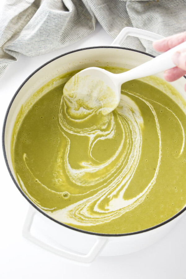 Adding cream to asparagus pea soup.