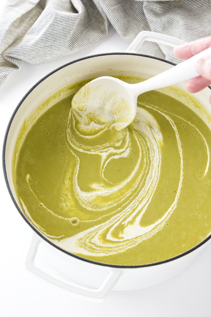 Adding cream to asparagus pea soup.