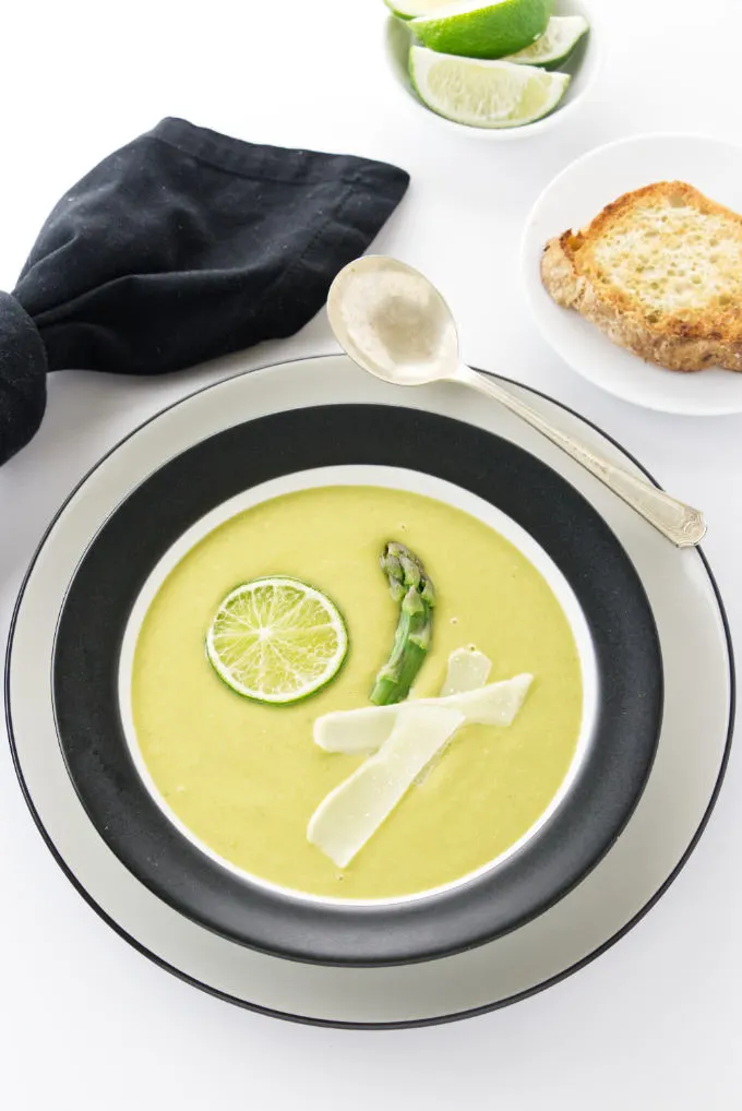 A bowl of asparagus pea soup with lime wedges.