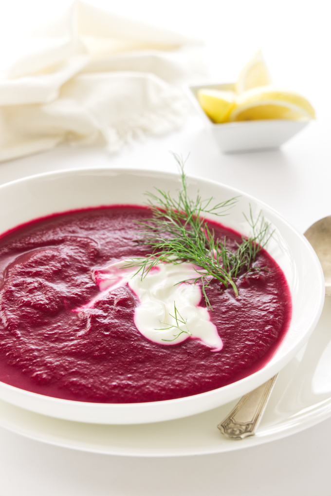 a dish of red beet soup garnished with cream and a fennel sprig