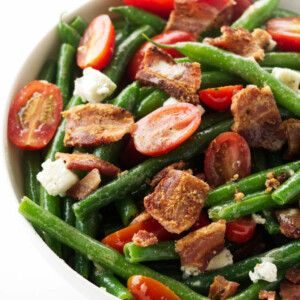 A large bowl of green bean salad with bacon and tomatoes.
