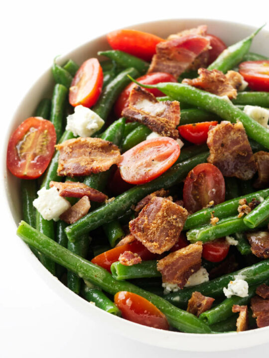 A large bowl of green bean salad with bacon and tomatoes.