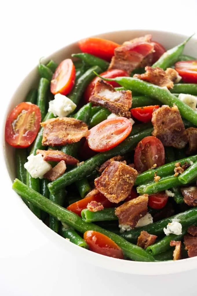 A large bowl of green bean salad with bacon and tomatoes.