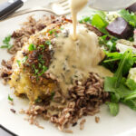 close up view of a serving of roasted chicken thigh and a pour of white wine sauce