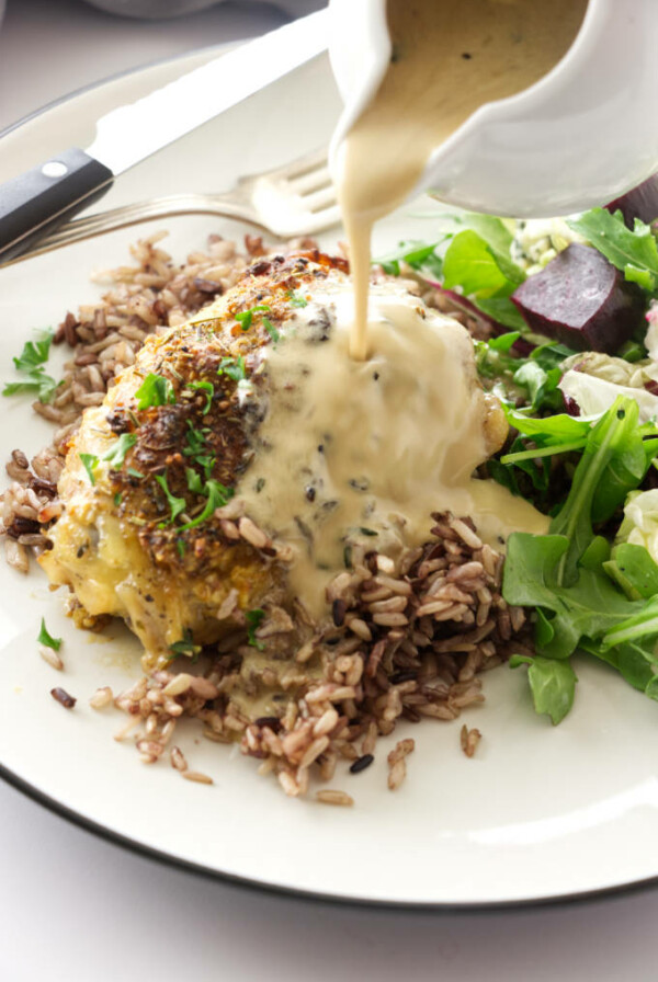 close up view of a serving of roasted chicken thigh and a pour of white wine sauce