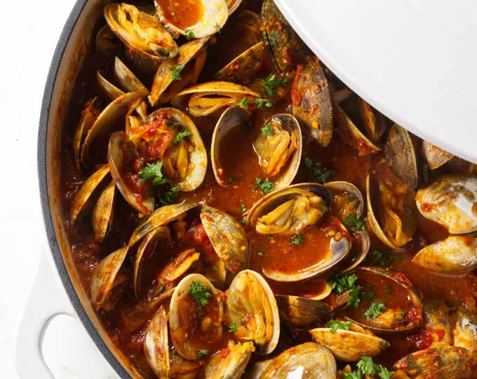 A large pot of clams in red sauce.