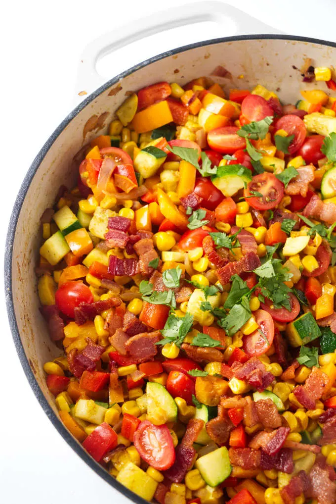 Corn succotash in a large skillet with bacon bits on top.