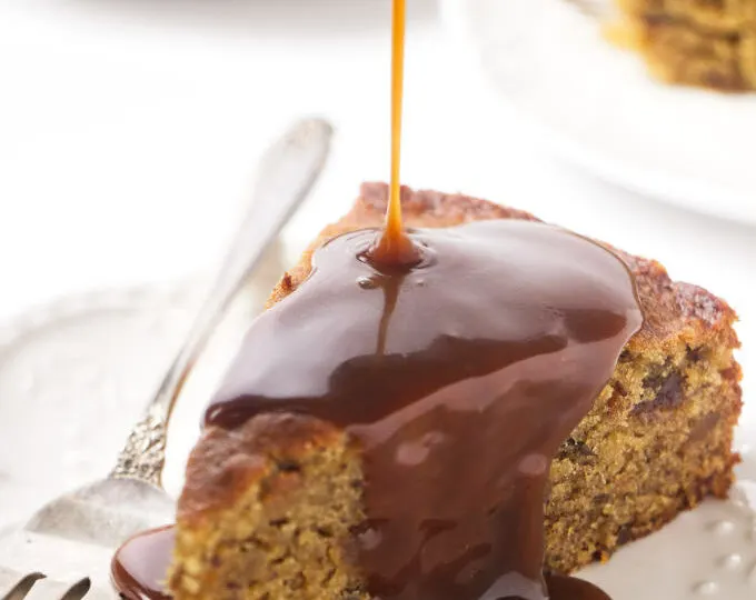 A slice of date cake with sticky toffee sauce being poured on top.