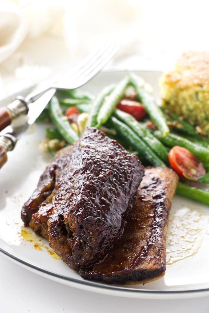 Beef rib on a dinner plate with green beans and cornbread.