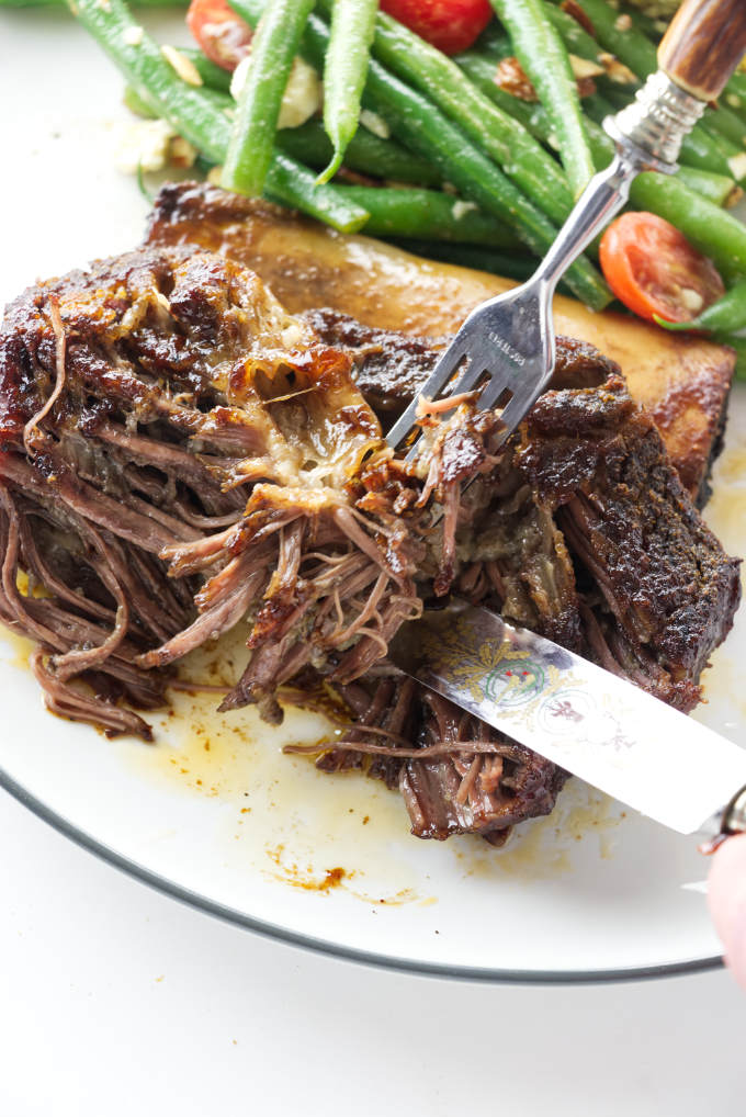 A tender beef rib being pulled apart with a fork.