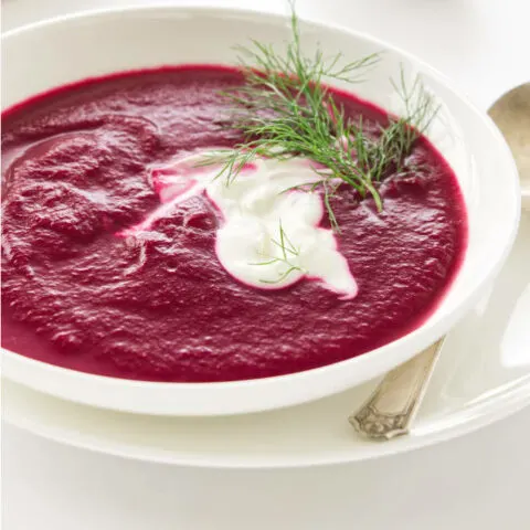 A bowl of roasted beet soup with a dill sprig.