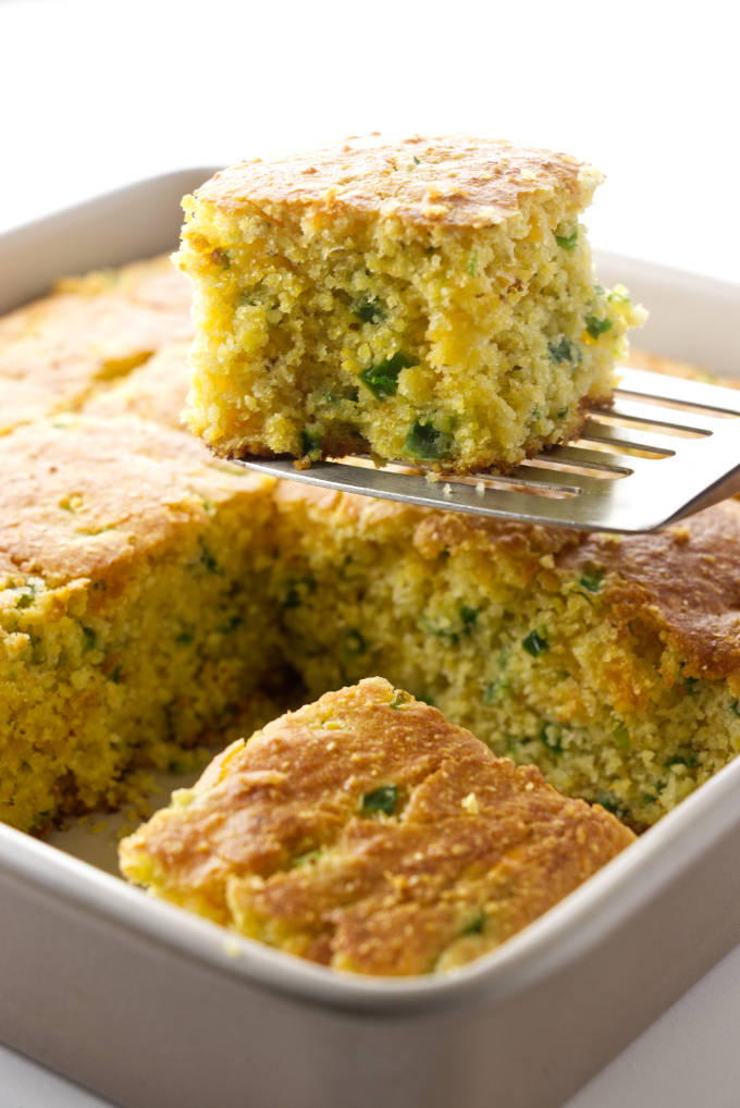 A slice of jalapeno cornbread being removed from a baking pan.