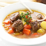 A bowl of lamb and vegetable soup with soup spoon