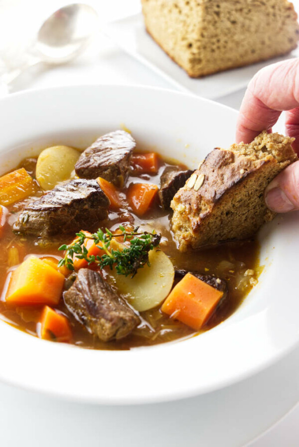 A serving of soup, a chunk of brown bread being dipped in the soup