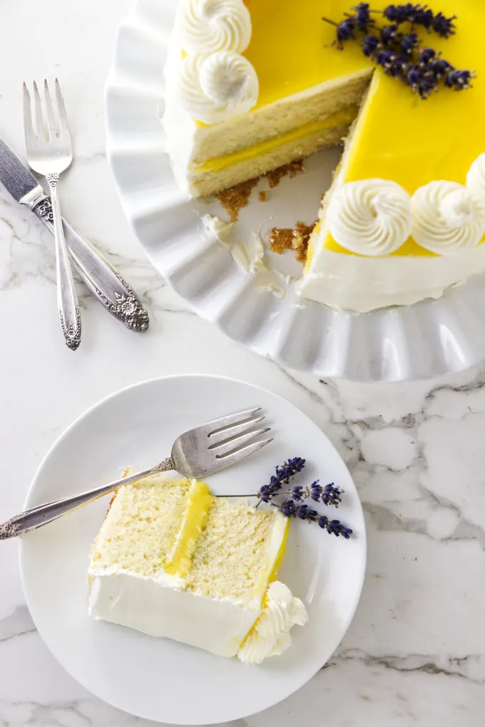 A lemon lavender cake on a cake plate with a slice of cake on a dessert plate.