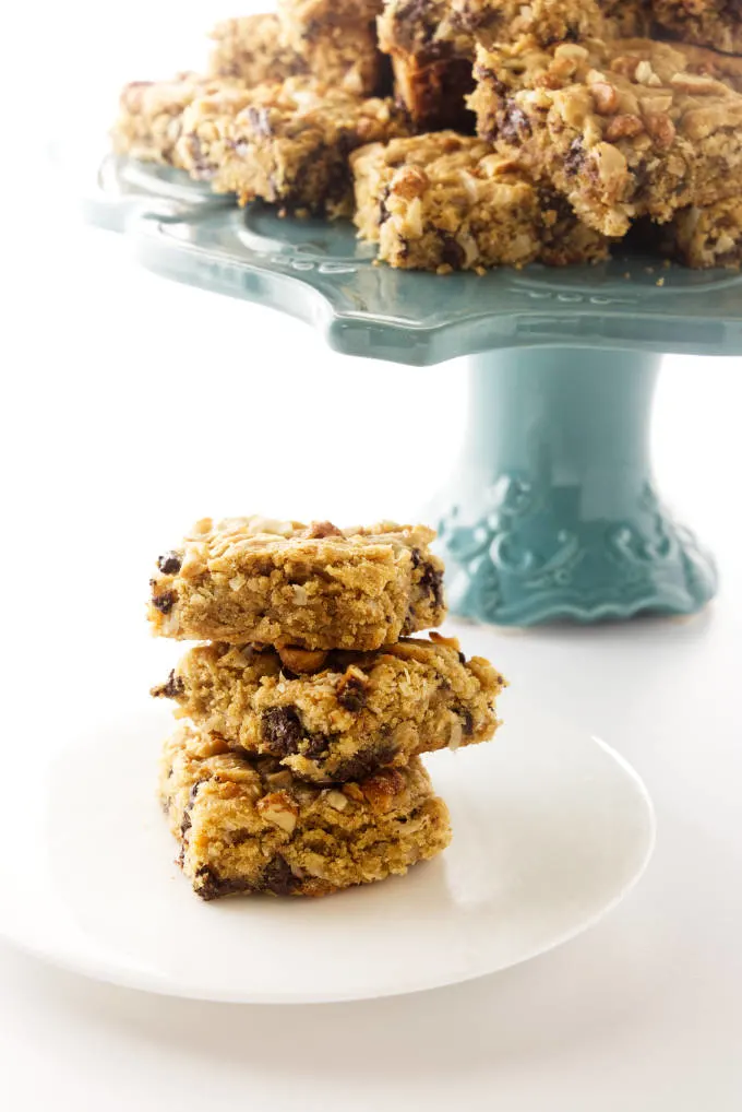 Peanut butter coconut bars on a dessert plate with a stack of cookie bars in the background.