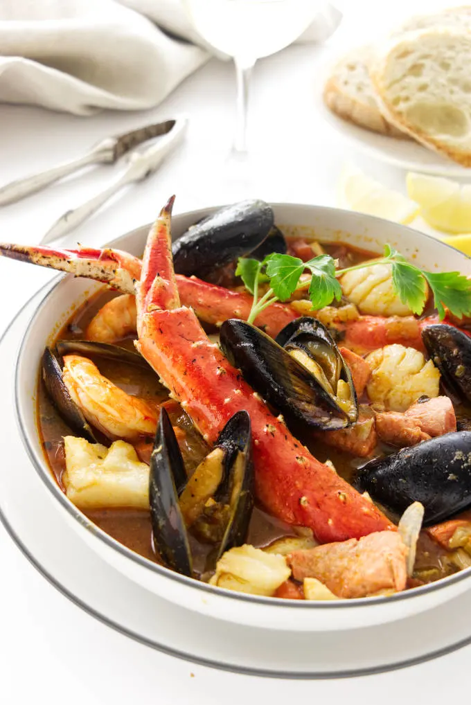 A serving bowl of seafood stew with king crab, shrimp, scallops, mussels, halibut, and salmon.