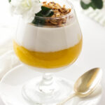 A serving of coconut-mango panna cotta garnished with toasted coconut and a flower