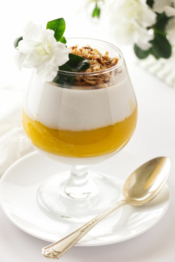 A serving of coconut-mango panna cotta garnished with toasted coconut and a flower