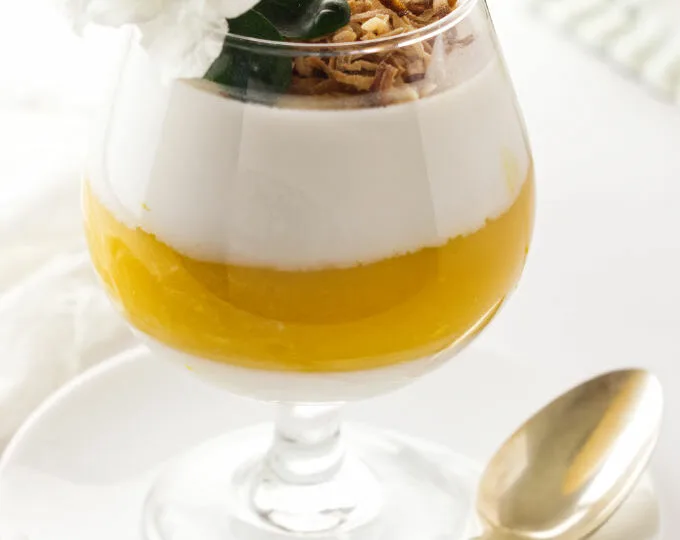 A serving of coconut-mango panna cotta garnished with toasted coconut and a flower