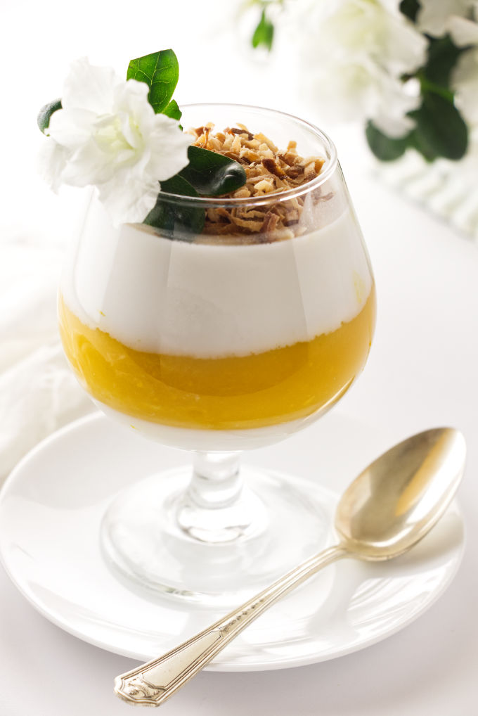 A serving of coconut-mango panna cotta garnished with toasted coconut and a flower