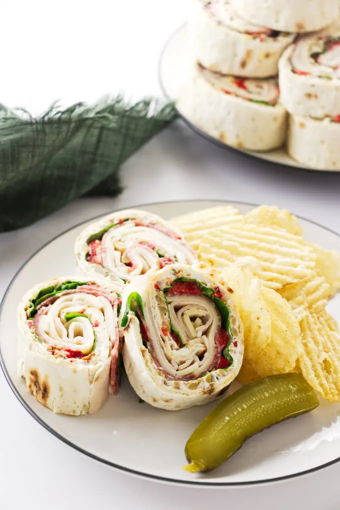 Three pinwheel appetizers on a plate with potato chips.