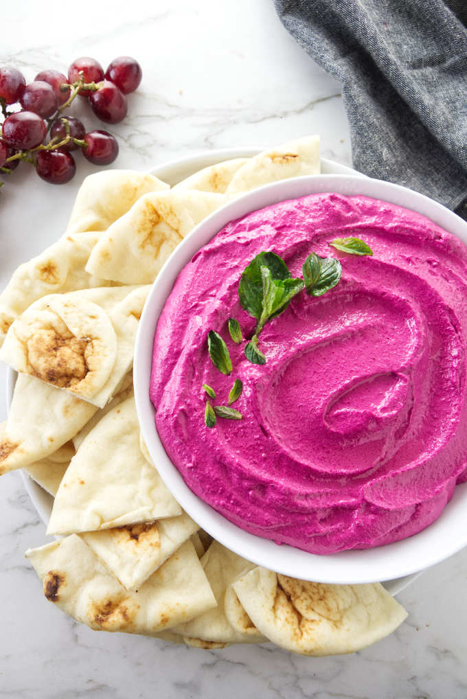 Red beet labneh with naan bread and grapes on the side.