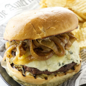 Caramelized onion burger with blue cheese and a side of potato chips.