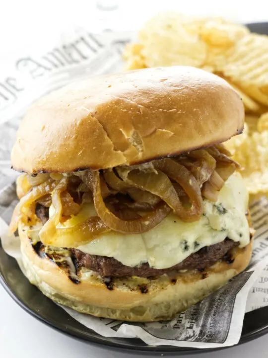 Caramelized onion burger with blue cheese and a side of potato chips.