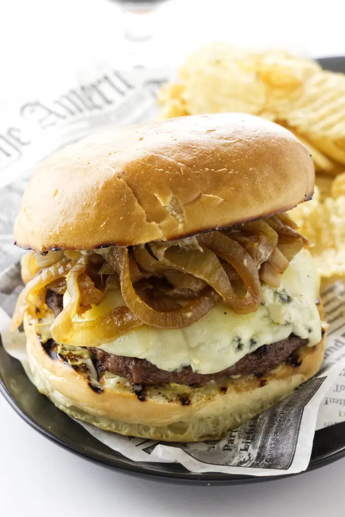 Caramelized onion burger with blue cheese and a side of potato chips.