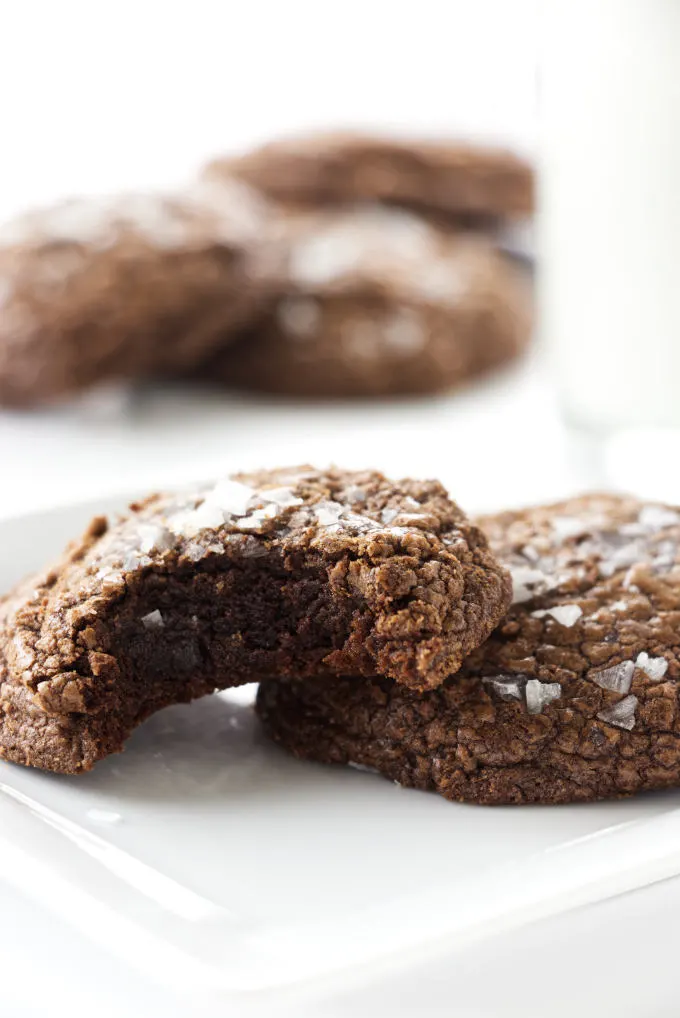 A plate of chocolate fudge cookies with a bite taken out of a cookie.