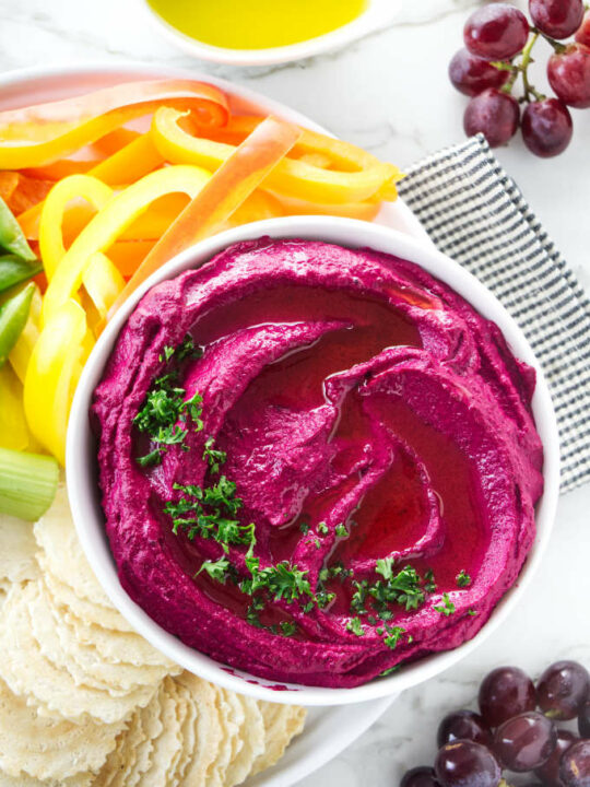 Beet hummus in a bowl with raw veggies on the side.
