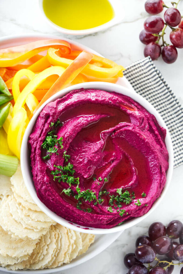 Beet hummus in a bowl with raw veggies on the side.