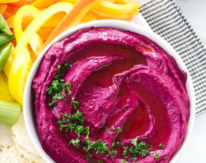 Beet hummus in a bowl with raw veggies on the side.